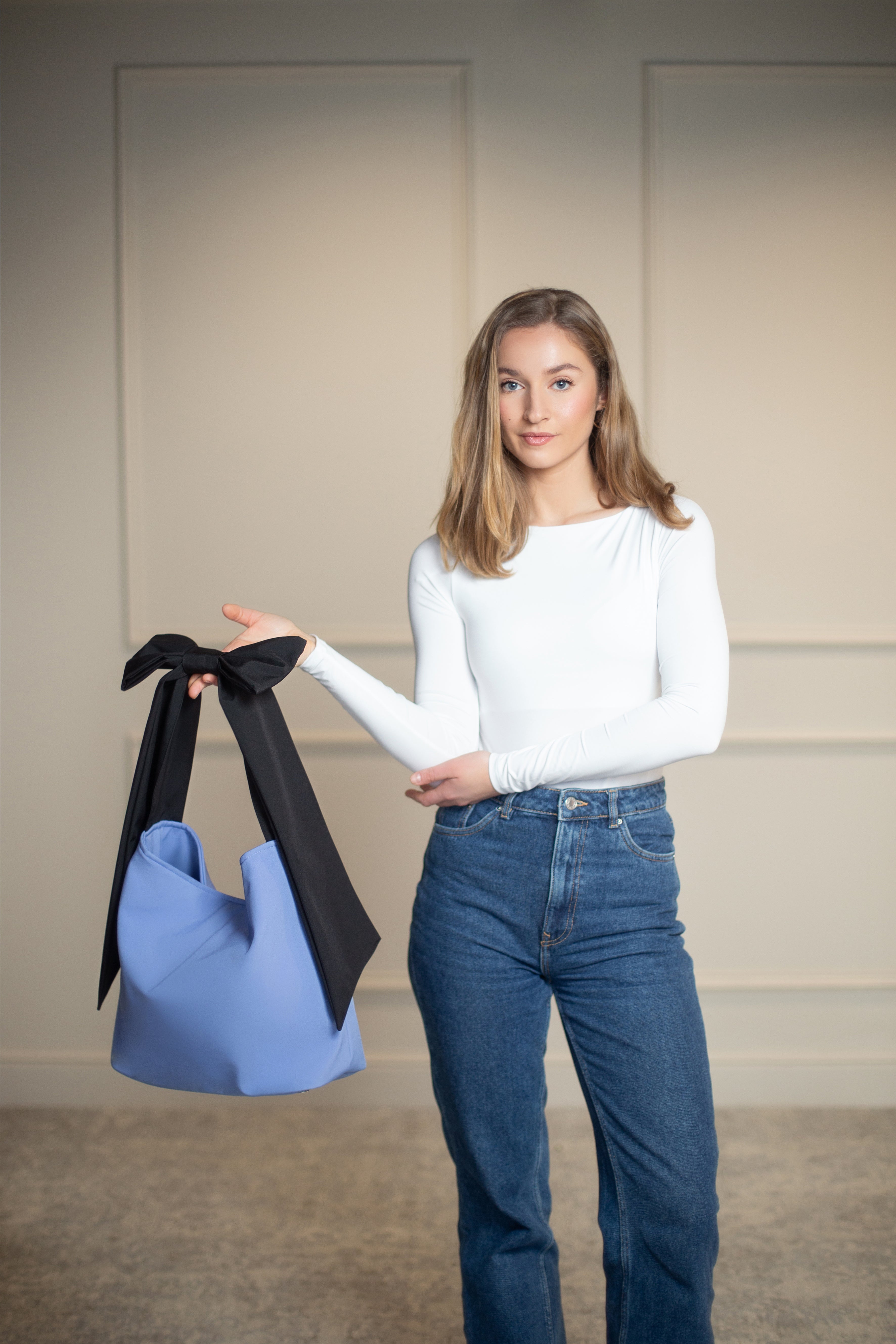 Minimalist soft blue tote with a black shoulder strap and subtle bow, offering both elegance and everyday practicality.
