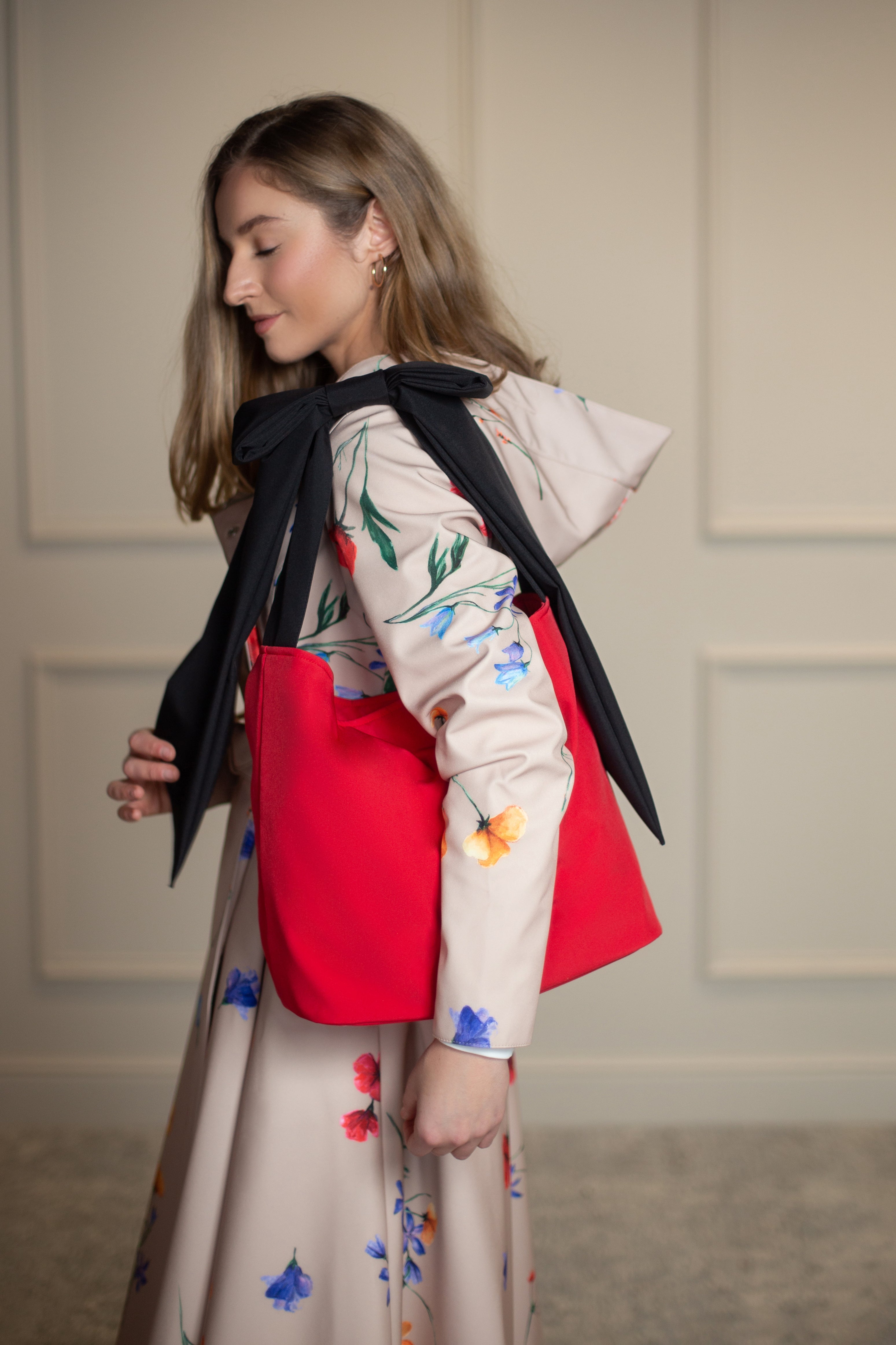 Bold red tote bag with black strap and bow detail, styled with the Spring Bloom coat; perfectly pairs with RainSisters outerwear.