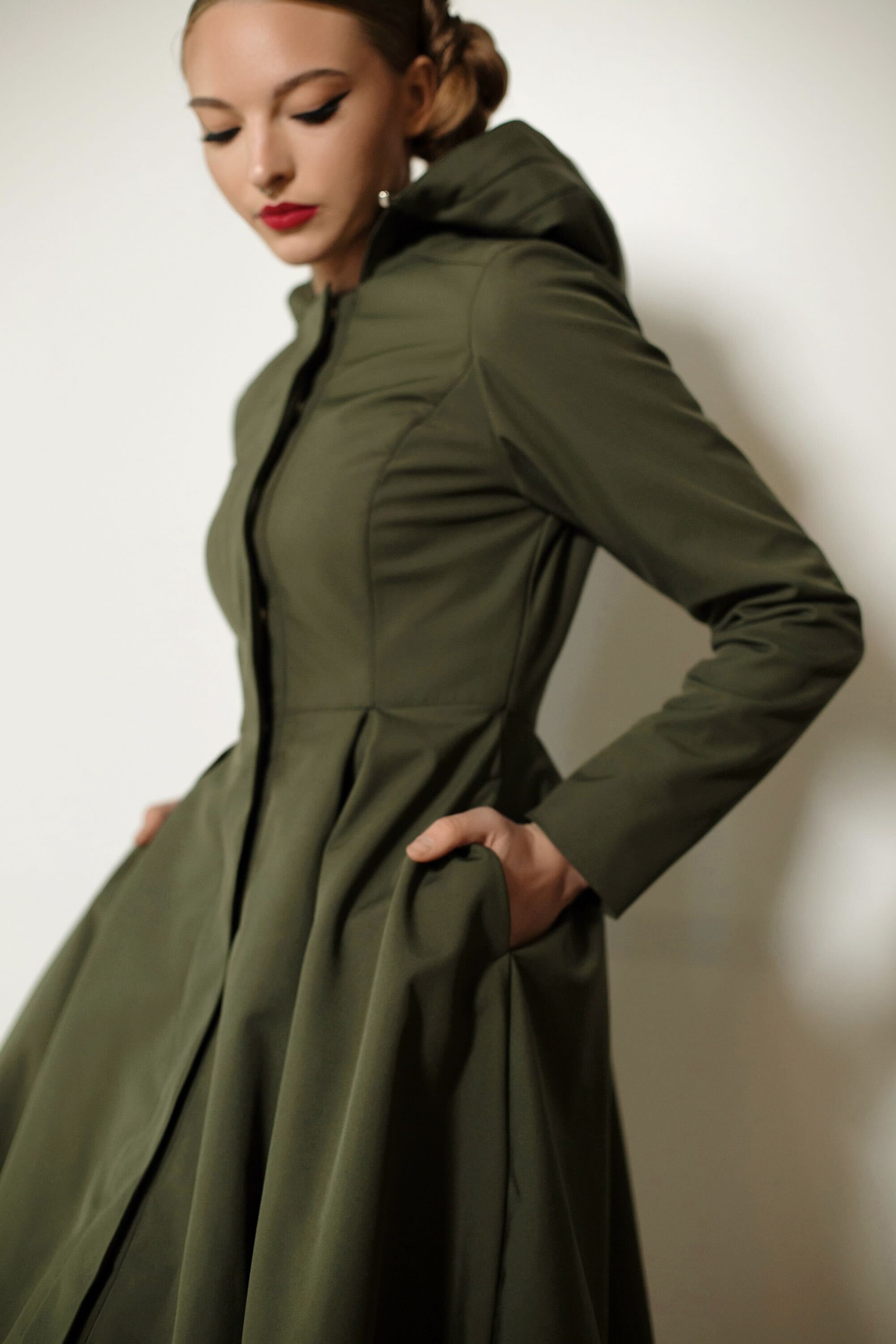 Folded Moss Green coat showcasing hidden pockets, elegant pleated skirt, and versatile women’s outerwear design.