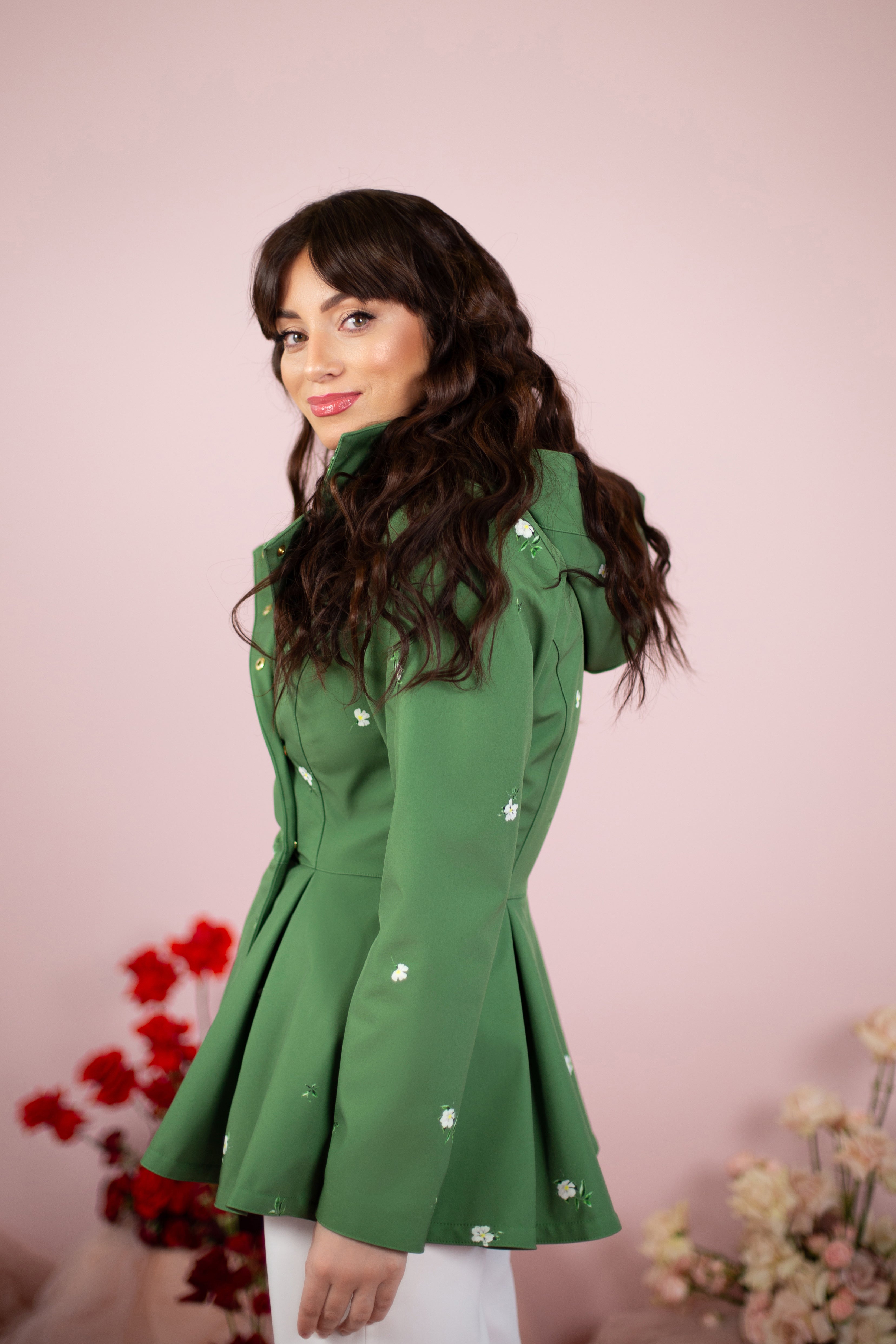 Woman wearing a green coat with floral details against a pink background
