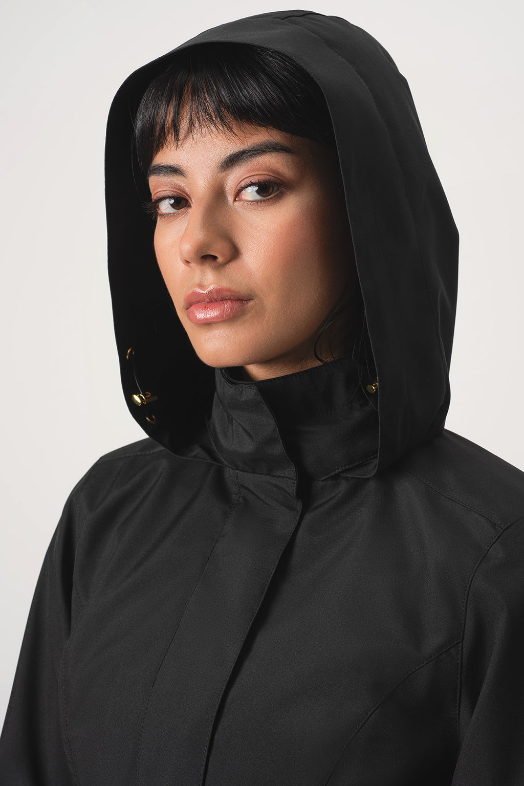 A close-up portrait of a woman wearing RainSisters black hooded jacket Black Sway against a light gray studio background.