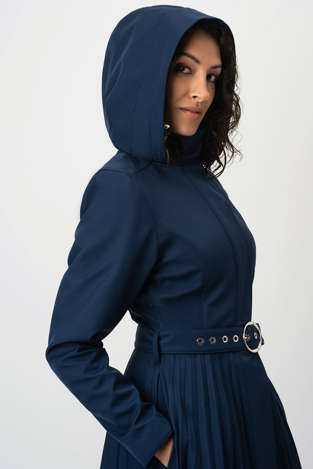 A woman wearing RainSisters navy blue hooded raincoat Blue Serenade with a matching belt and silver buckle, shown from a side profile against a light gray studio background.