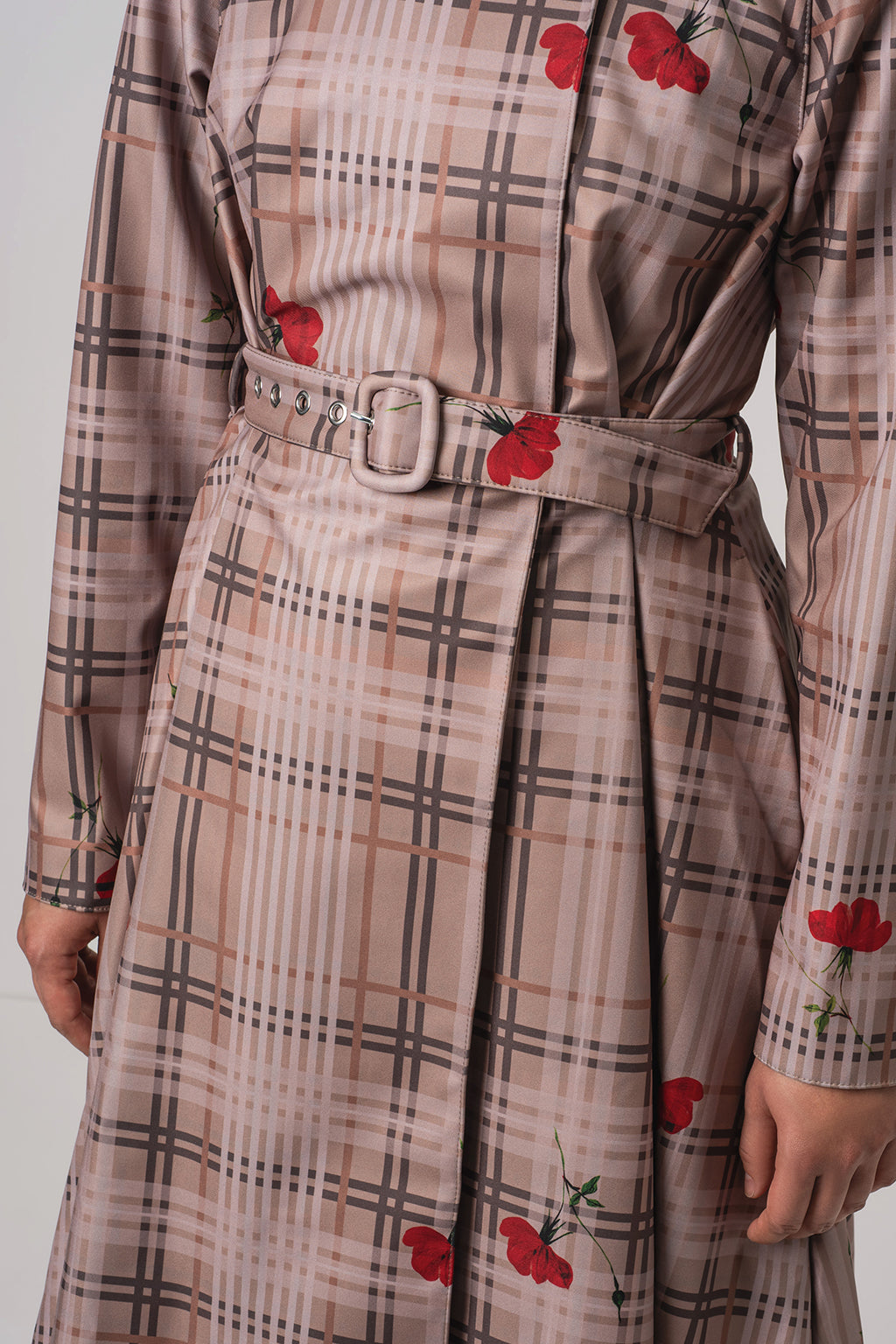 A close-up of RainSisters long-sleeve plaid raincoat Blush of the Crown with a matching belt and red floral print, shown on a model against a light gray background.