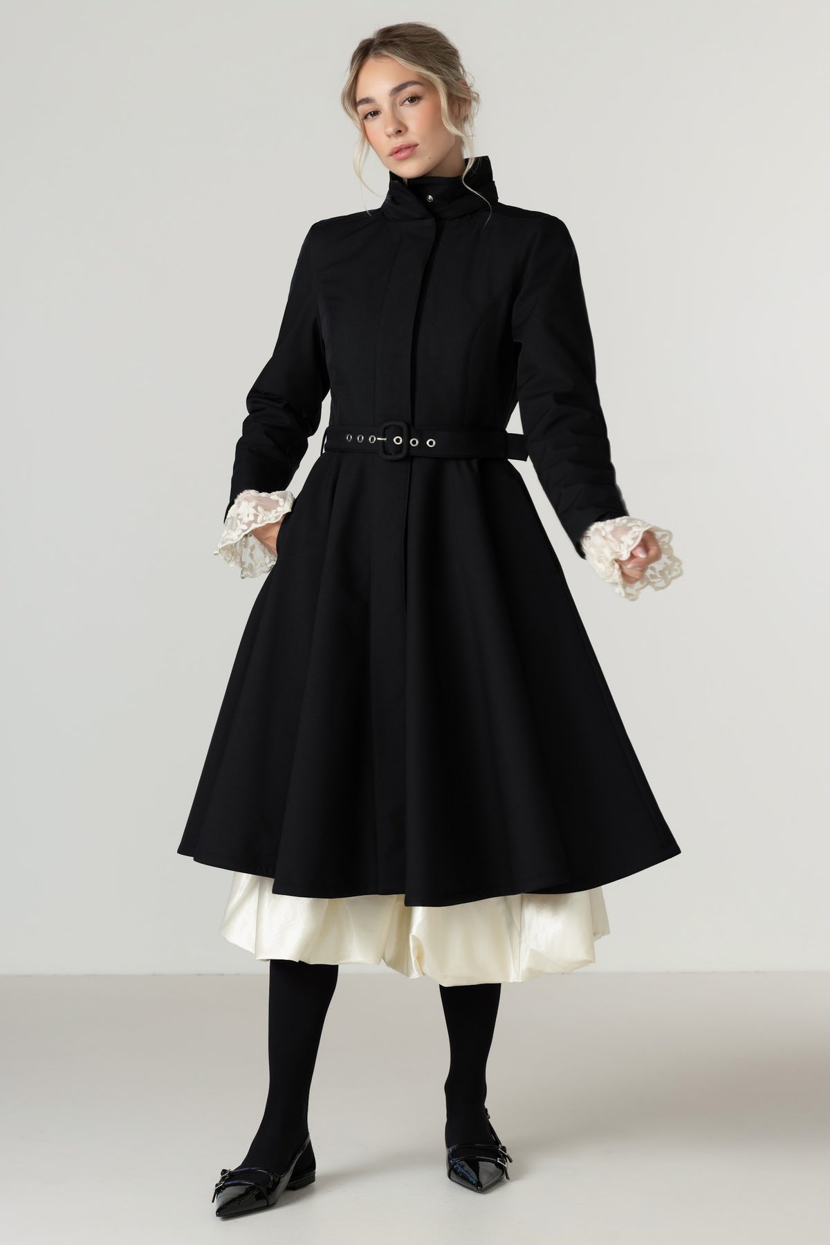 A woman models a Rainsisters black high-neck, long-sleeve A-line winter coat with a matching waist belt.