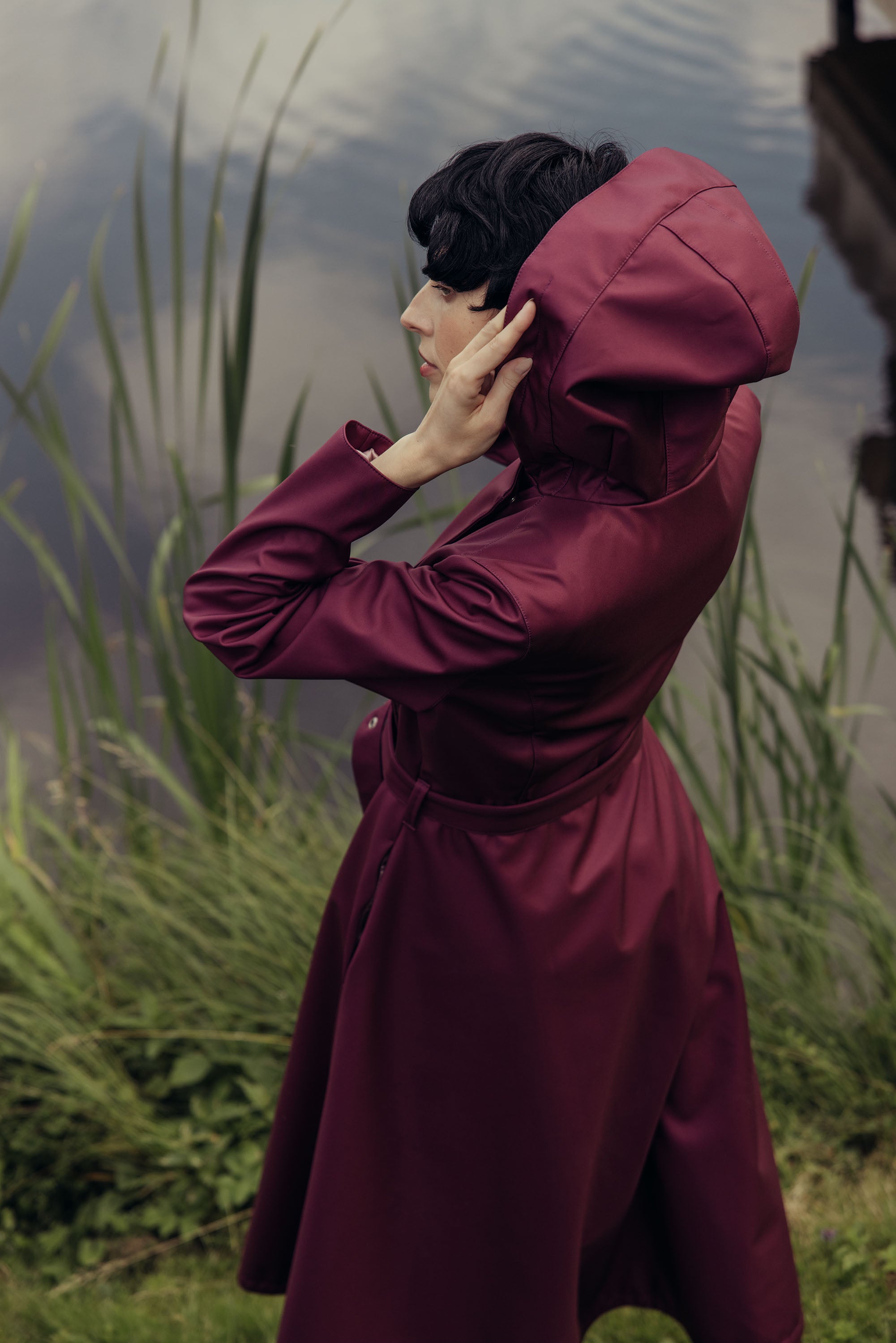 Women's deep burgundy double-breasted trench coat with an effortlessly elegant silhouette captured outdoors.