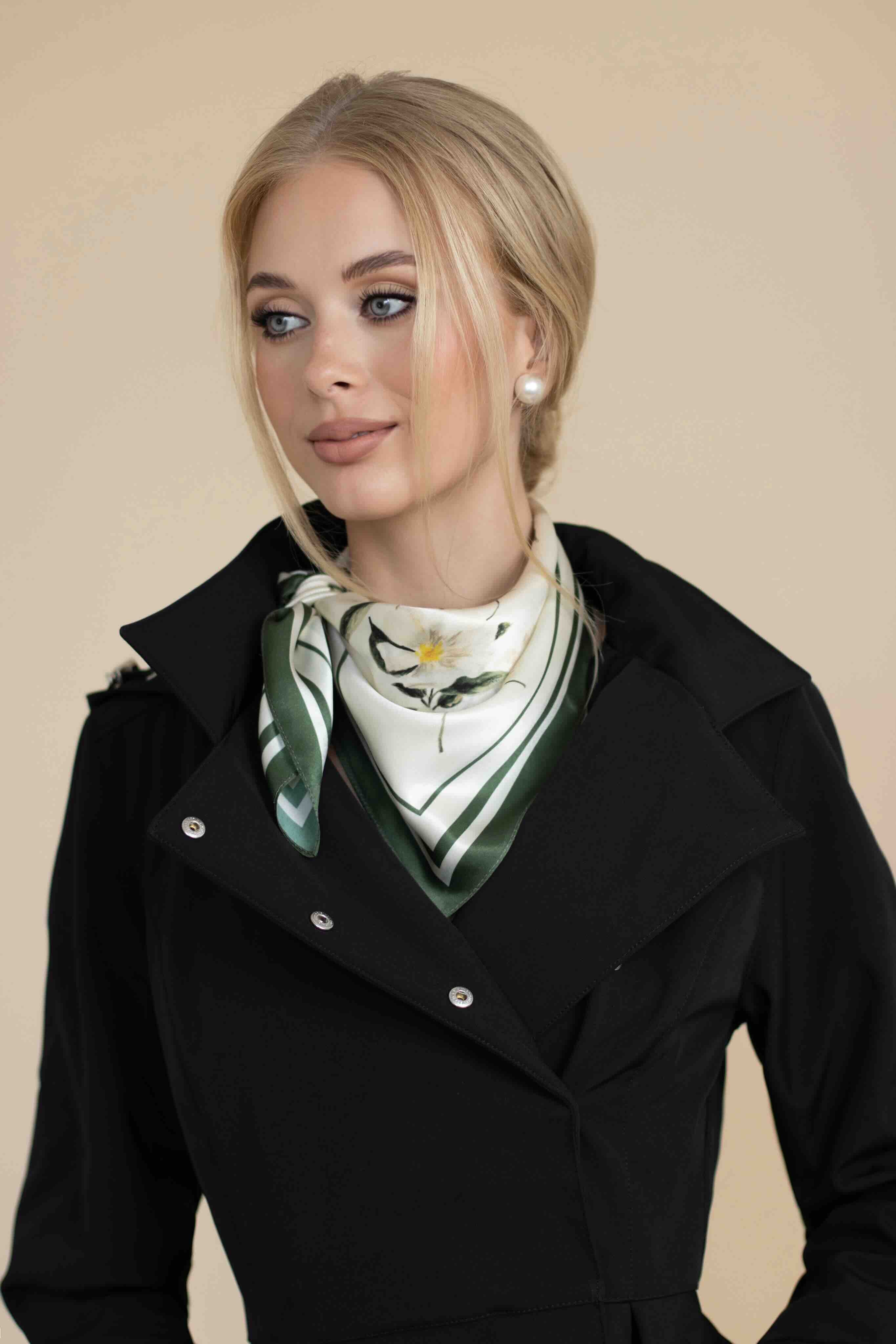 Woman wearing a black coat with a green and white patterned scarf against a beige background