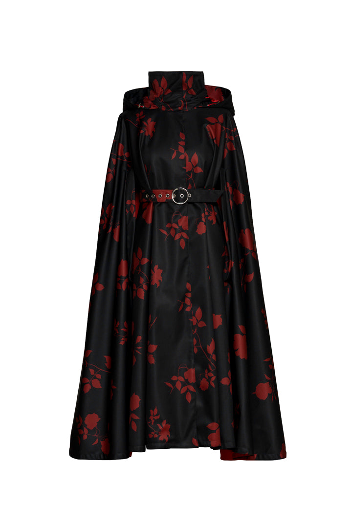 A black cape coat with red rose print by RainSisters featuring a high collar, a matching belt with a round silver buckle, and a flared skirt, shown against a plain white background.