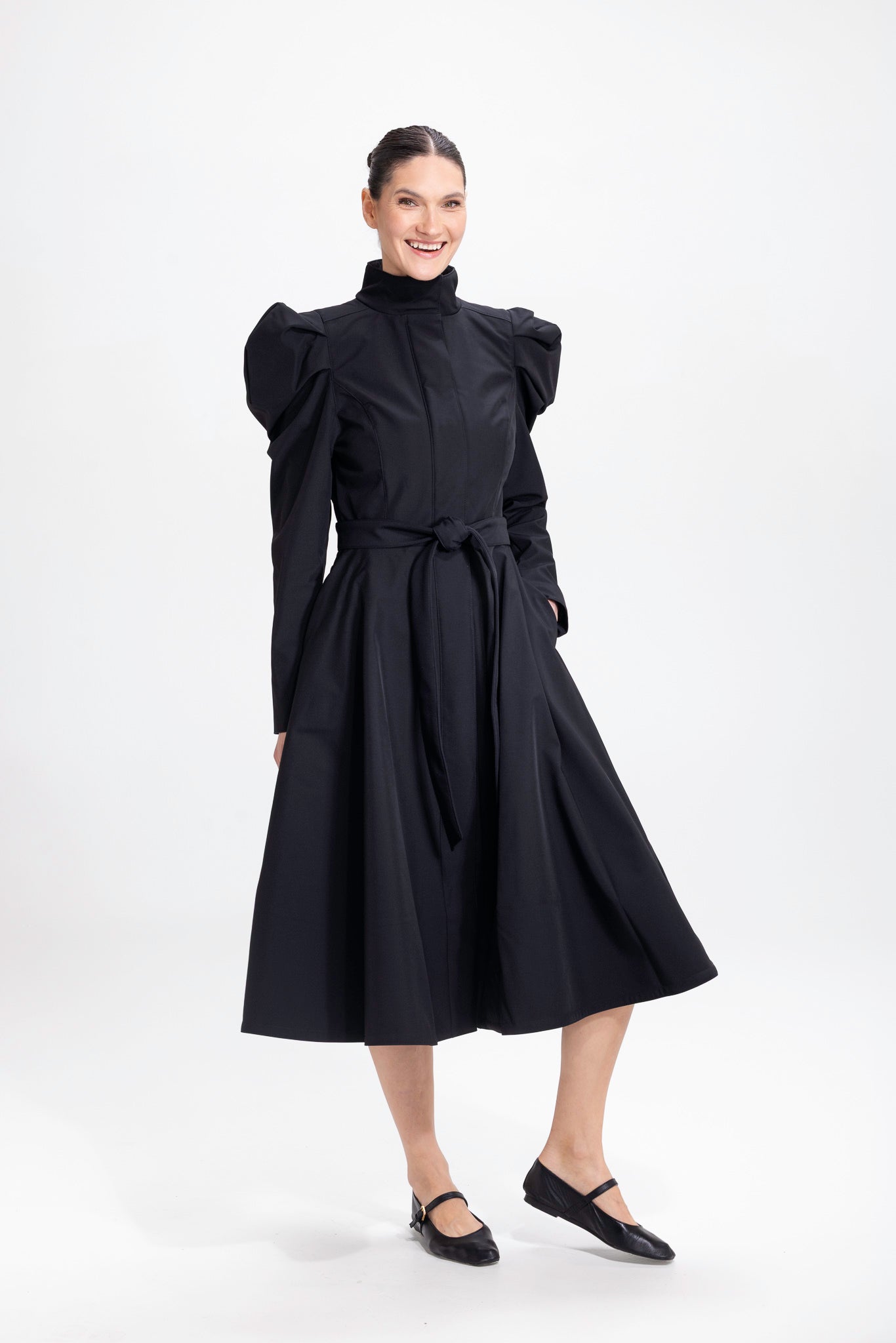 Model in motion wearing elegant black coat with balloon sleeves and flowing A-line skirt