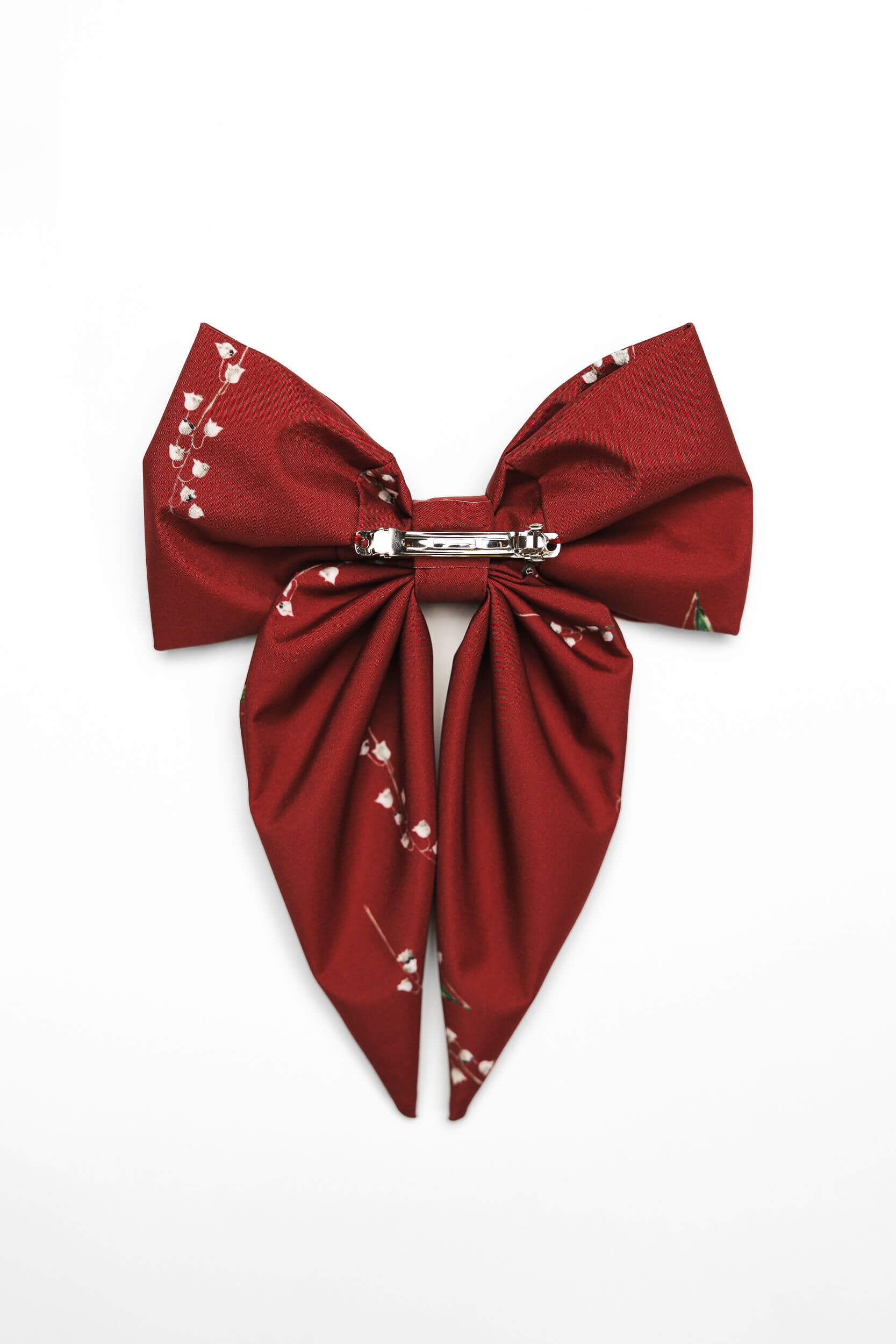 Red bow hair clip with white floral pattern on a white background back view.
