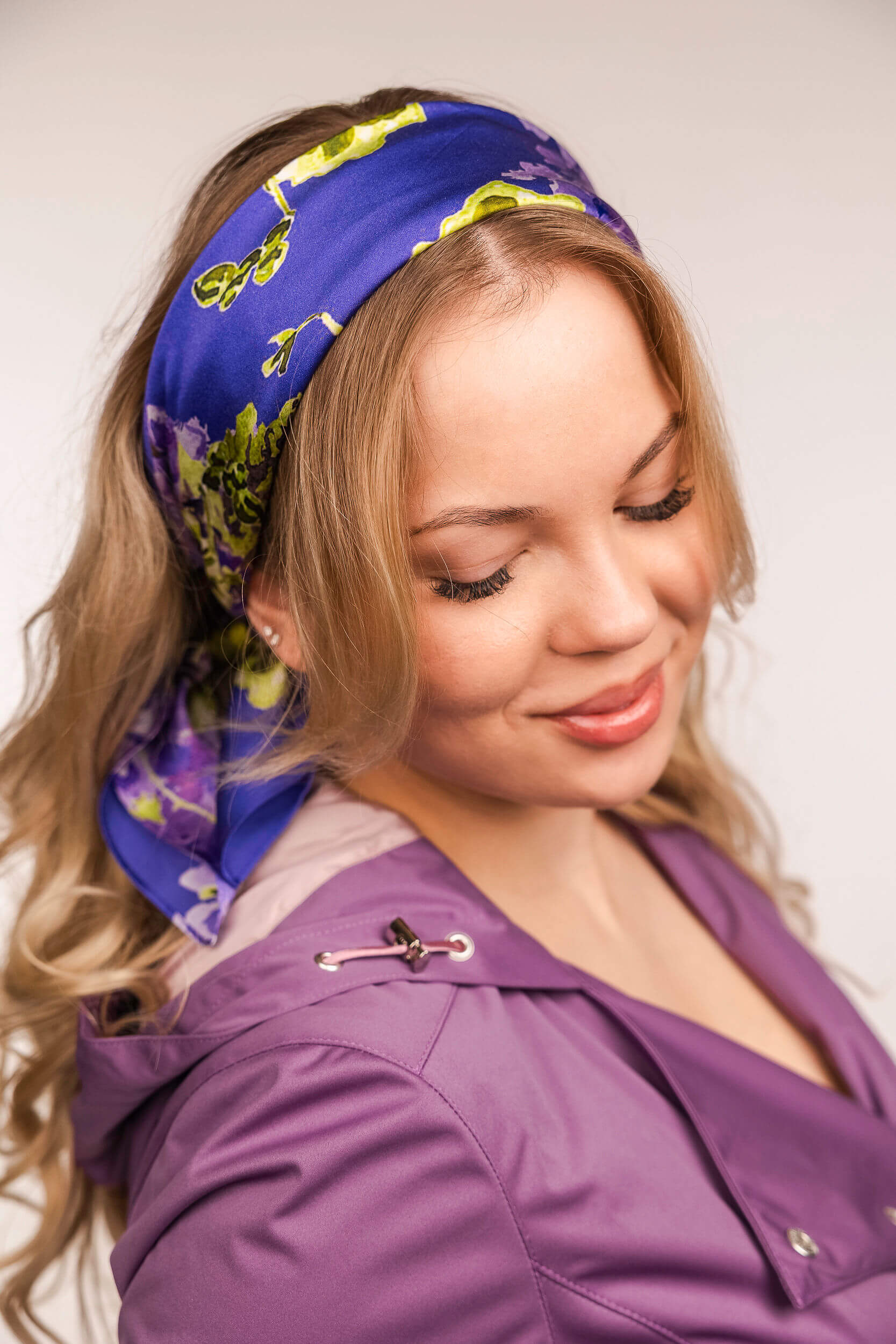 Woman wearing a purple headscarf with floral patterns on a plain background