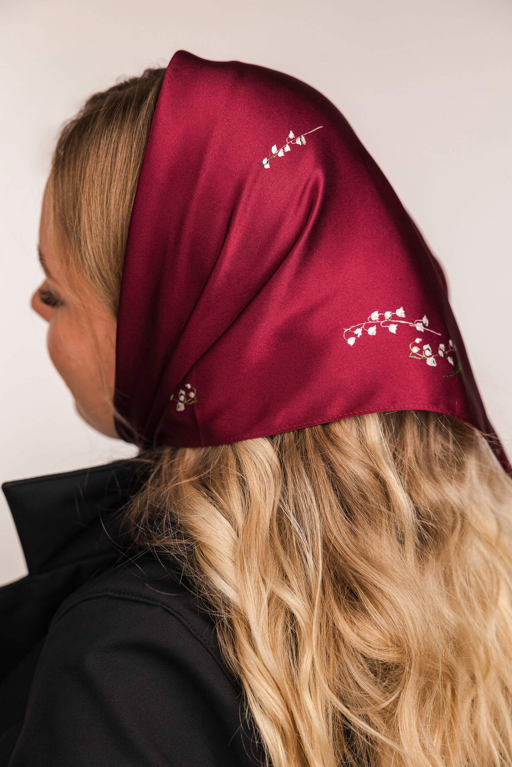 Model wearing a burgundy headscarf with floral print on a plain background