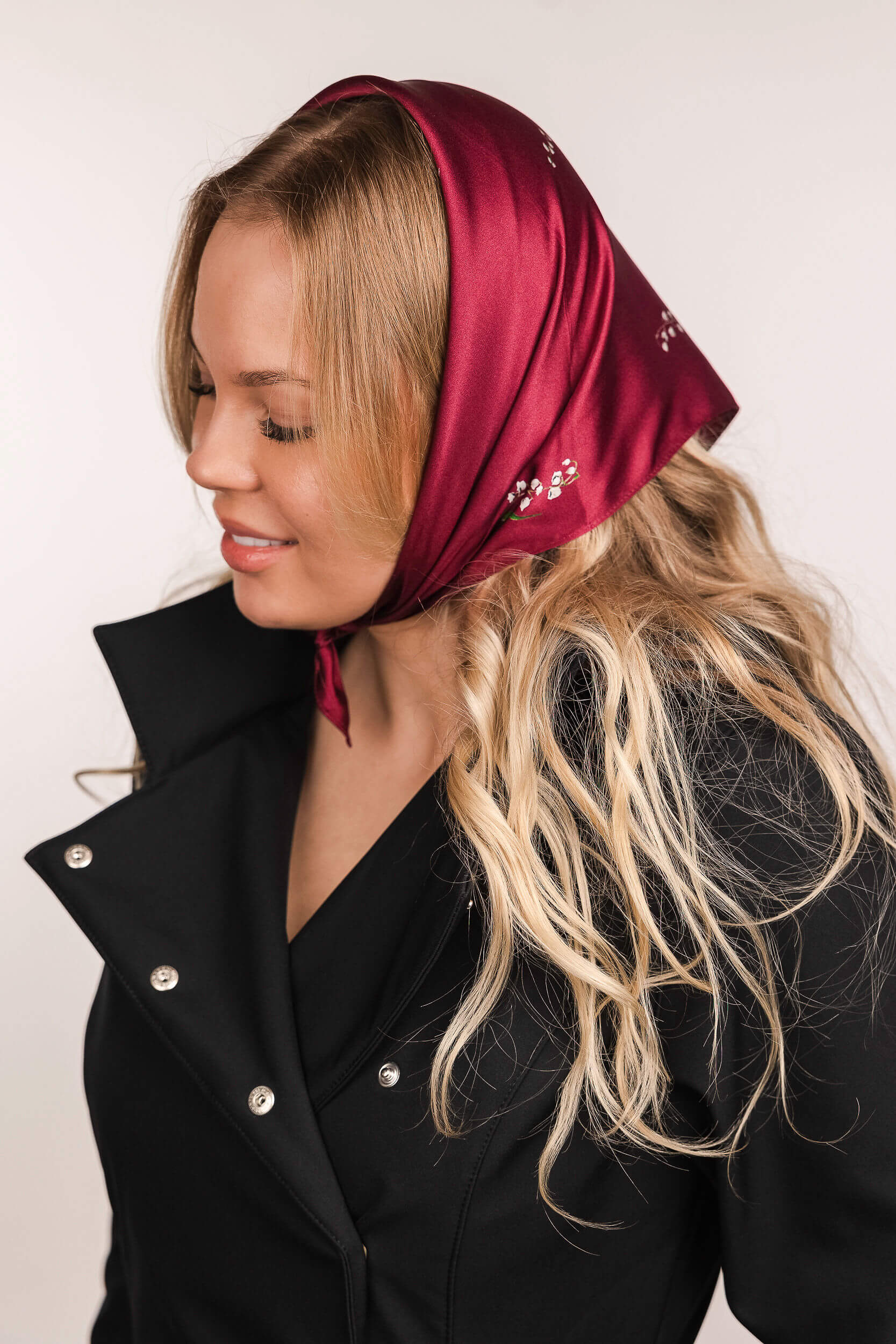 Woman wearing a red headscarf with floral print and a black coat on a white background