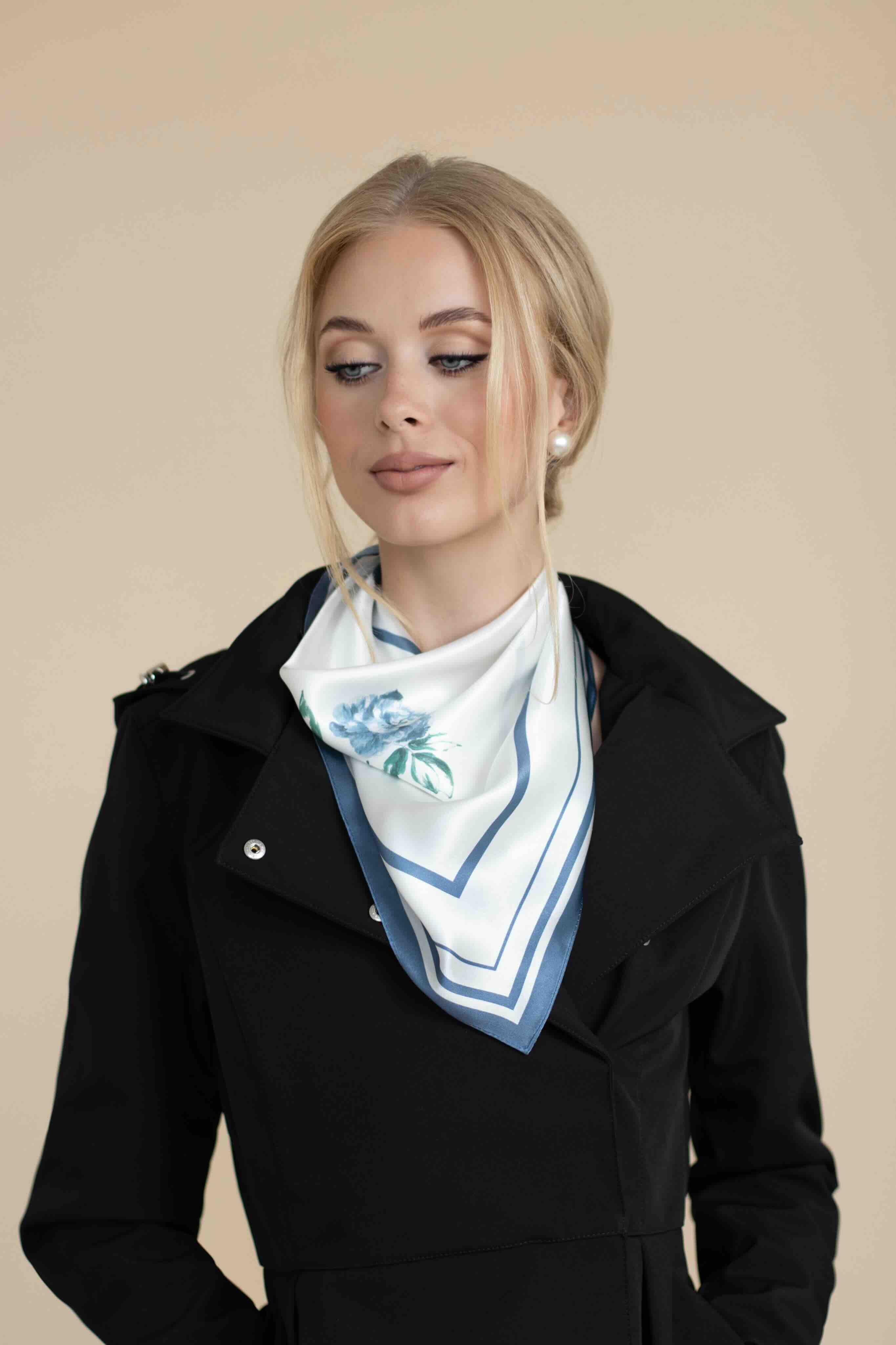 Woman wearing a black coat with a white scarf featuring blue floral pattern on a beige background