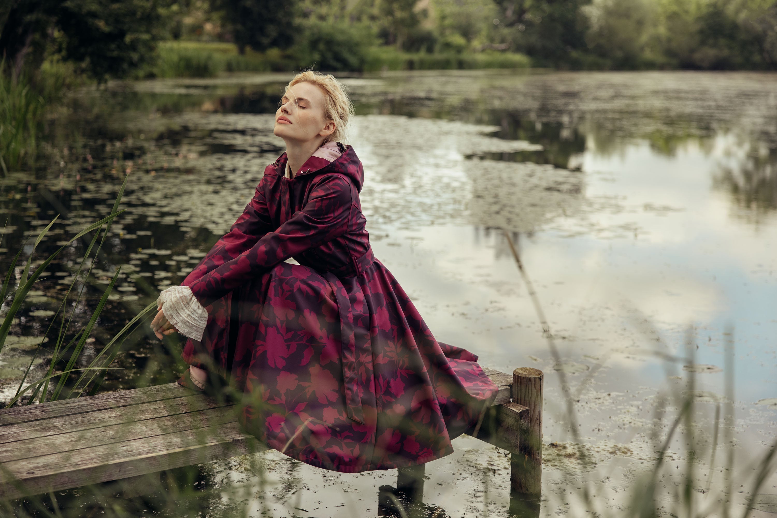 A model sitting wearing RainSisters waterproof coat Peony Velvet in dark purple with burgundy colored flower print