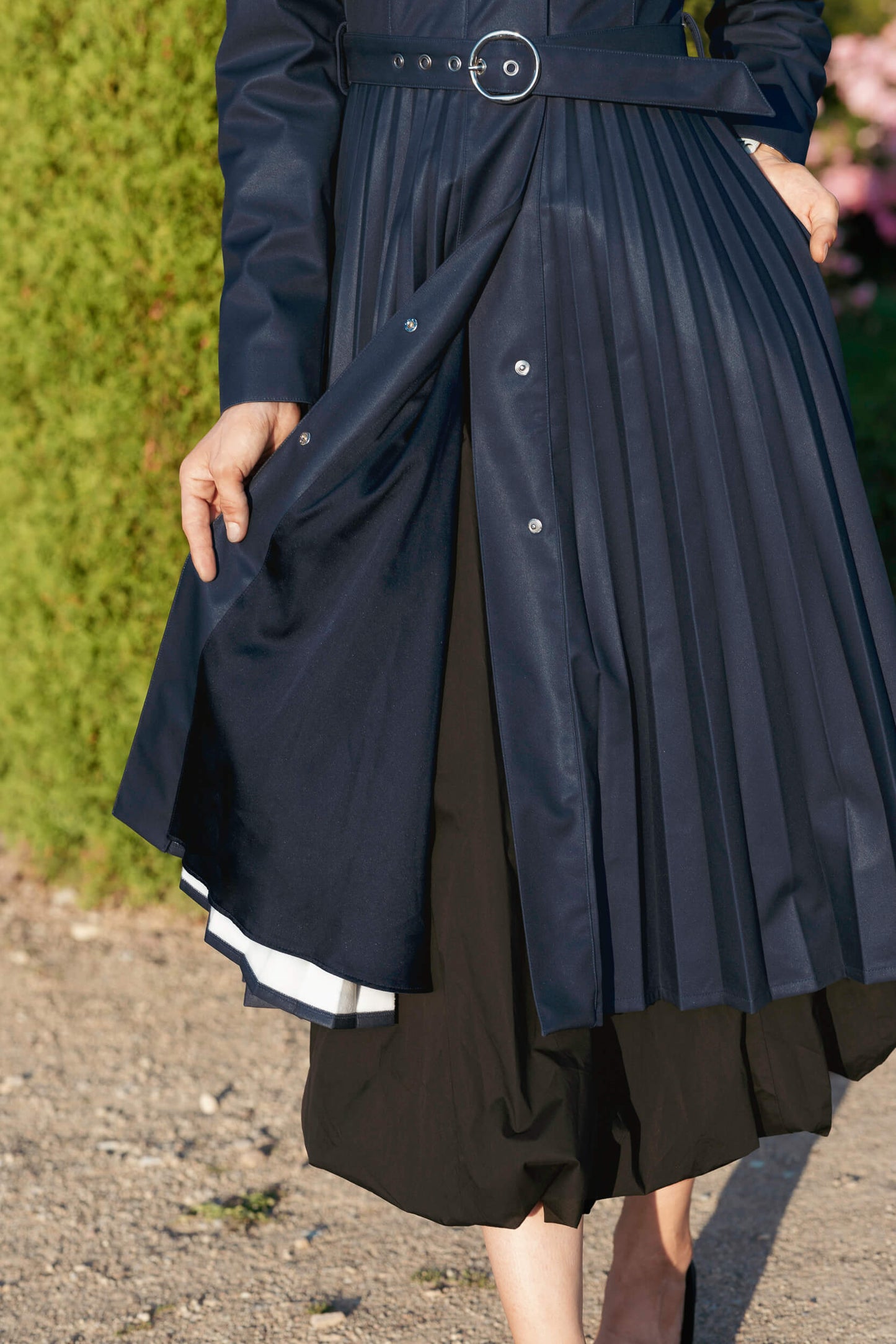 Blue pleated coat with a belt being worn outdoors.