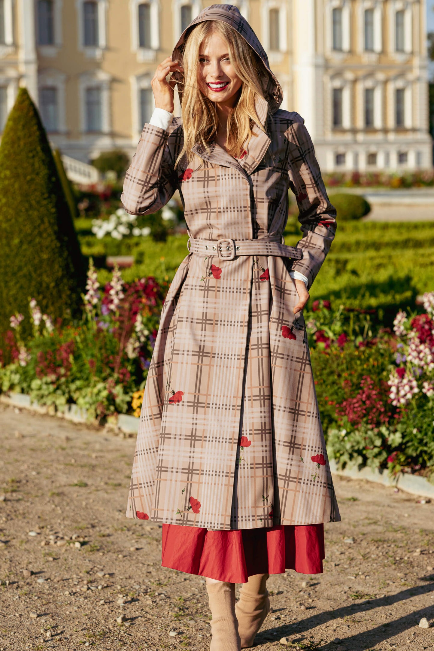 Woman in a plaid coat with red accents standing in a garden.