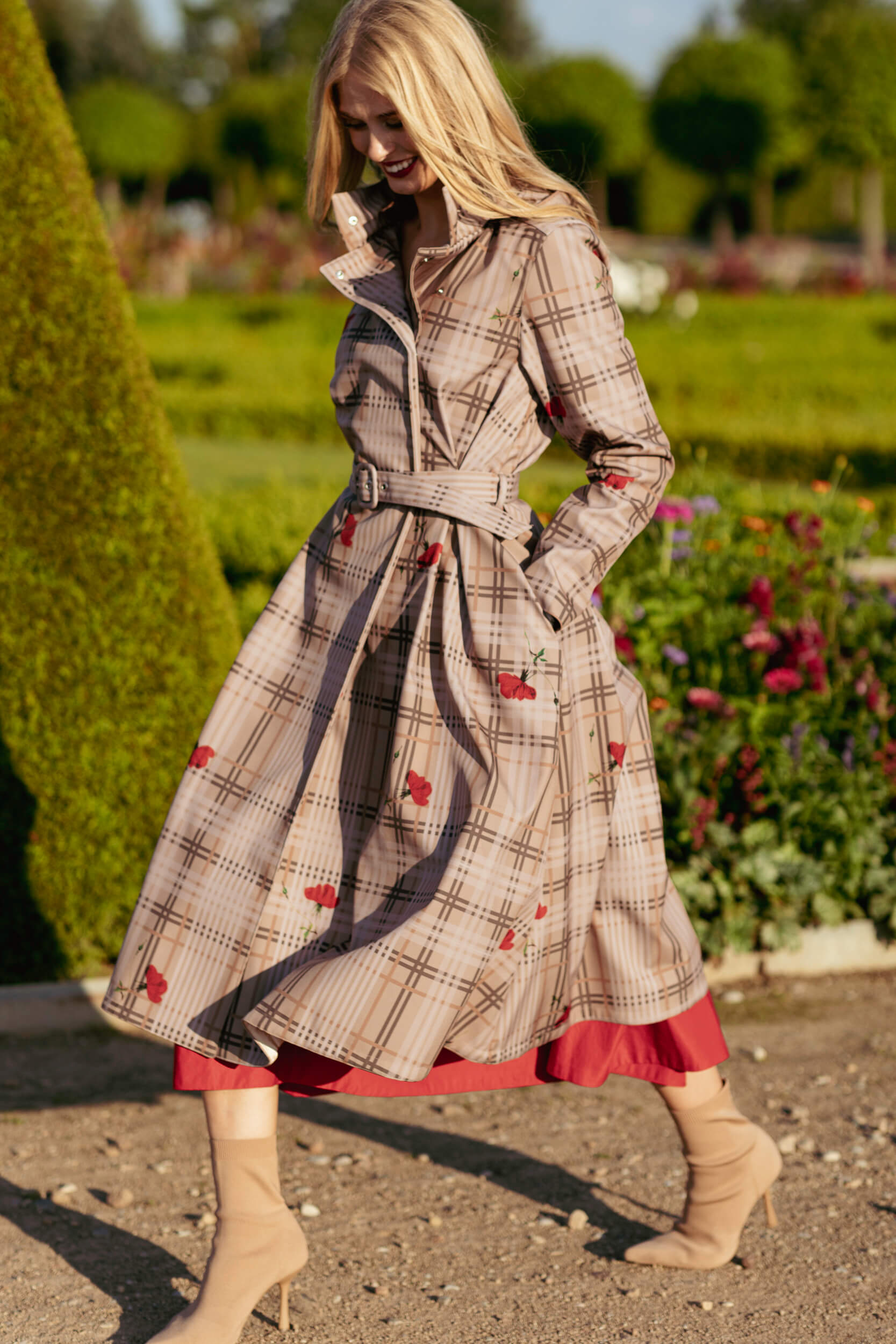 Woman wearing a plaid beige coat with red accents in a garden setting