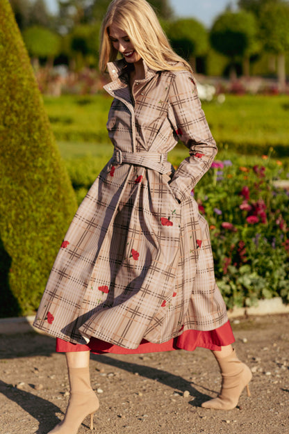 Woman wearing a plaid beige coat with red accents in a garden setting