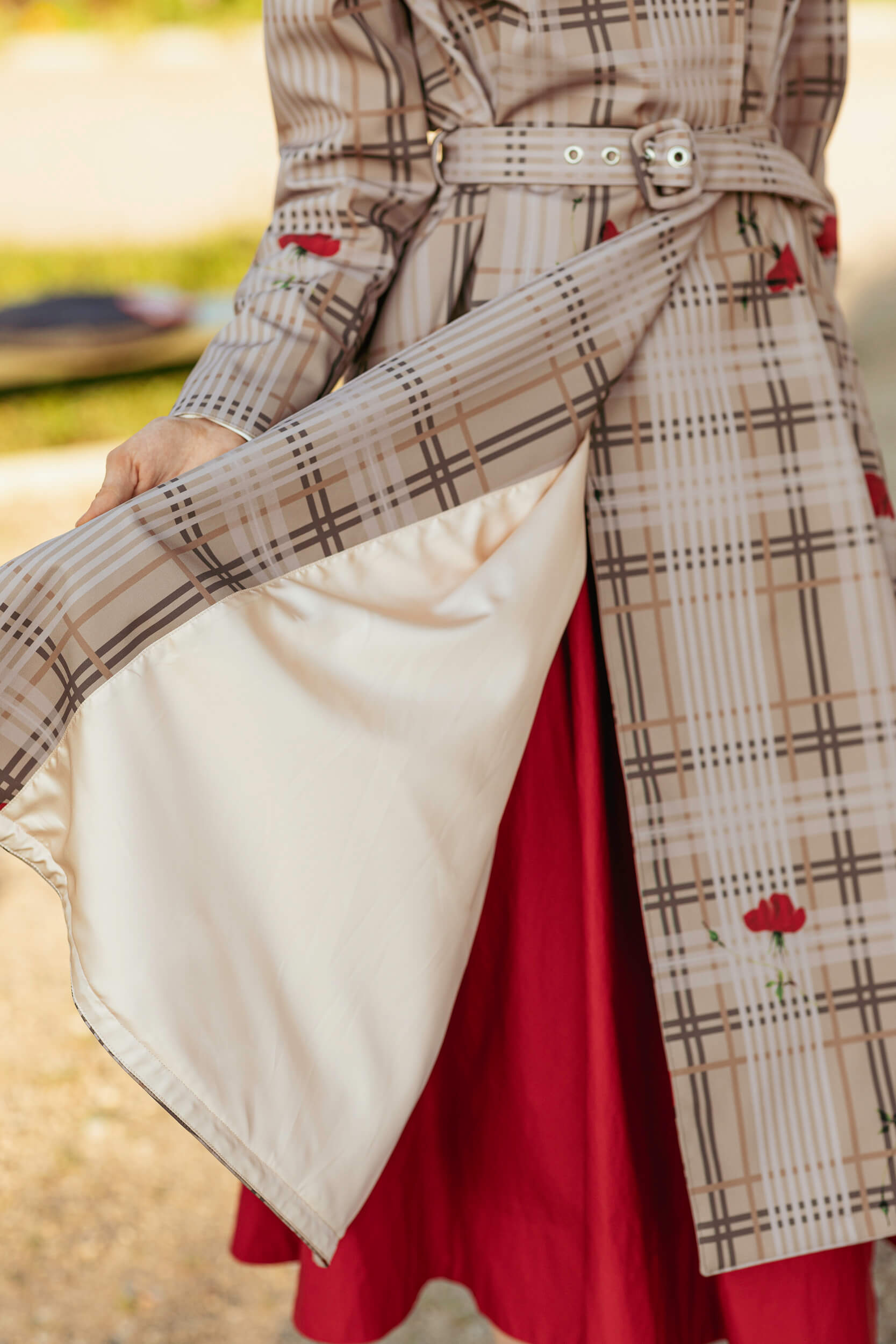 Model wearing a plaid coat with a belt, and red skirt outdoors.