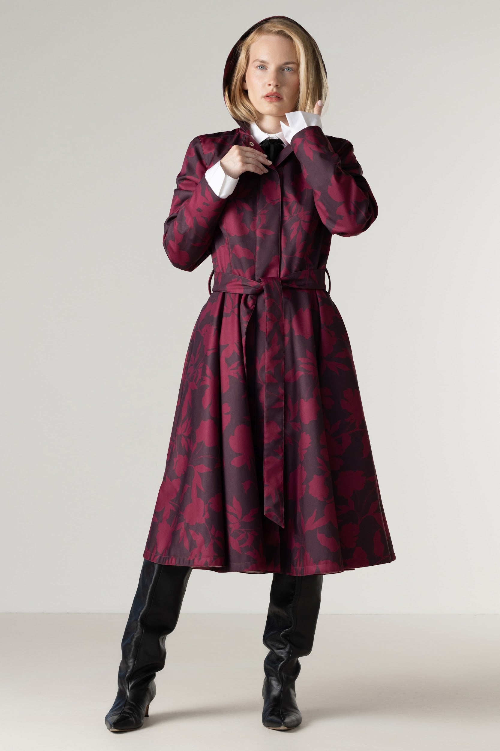 Full-length view of a women's burgundy floral fit and flare coat with a removable hood, flowing full circle skirt, and matching tie belt.