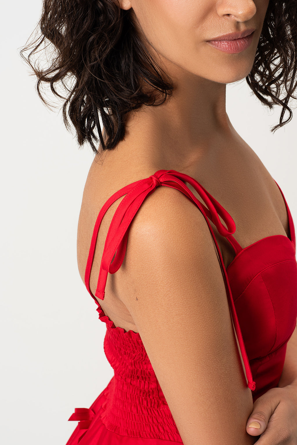 Close-up of a model wearing RainSisters bright red strapless dress Little Red Bows  with tie-shoulder straps and a smocked bodice, shown against a plain light gray background.