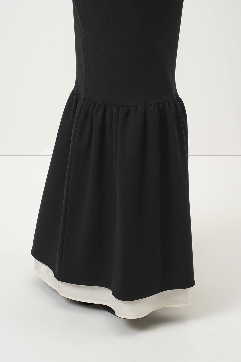 A close-up of RainSisters black dress Quiet Elegance with a flared ruffled hem, shown against a clean white studio background.