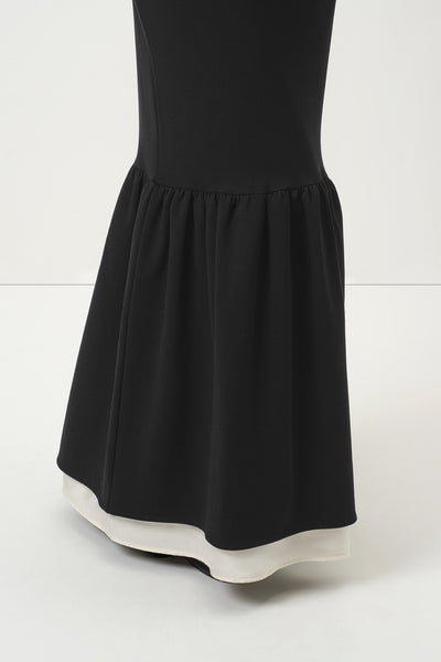 A close-up of RainSisters black dress Quiet Elegance with a flared ruffled hem, shown against a clean white studio background.