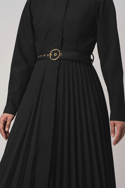 RainSisters black long-sleeve pleated trench coat Black Sway with a matching waist belt and a prominent gold-tone circular buckle, shown on a model against a light gray background.