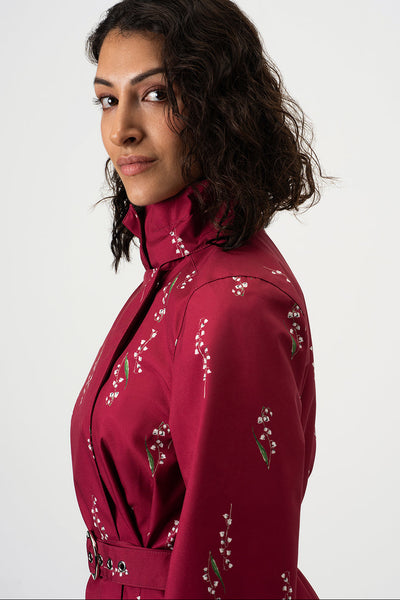 A woman with dark curly hair is shown in profile wearing RainSisters burgundy high-neck jacket Crimson Lily with white floral details, set against a plain light gray background.