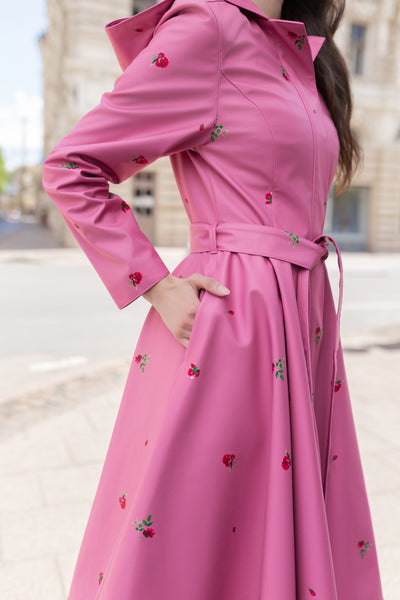 A woman wearing RainSisters pink raincoat Raspberry Sorbet with small red and green floral print, standing outdoors on a city street.
