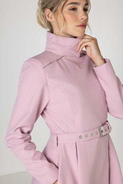 A woman wearing a light pink long-sleeve coat by RainSisters with a high mock neck, structured shoulders, and a matching waist belt with silver-tone buttons, shown against a plain light background.