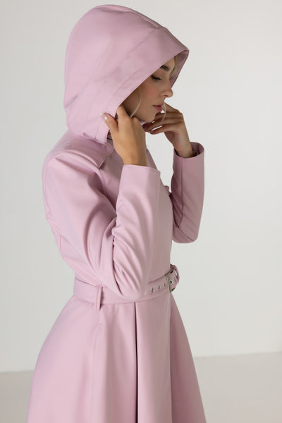A woman wearing RainSisters light pink hooded longline coat Rosie Bow with a matching belt, shown in profile against a plain light gray studio background.