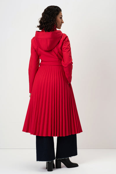 A model shown from the back wearing RainSisters bright red hooded coat Scarlet Waltz with a pleated skirt, paired with dark wide-leg pants and black boots, against a plain white studio background.
