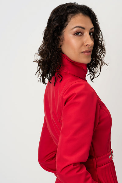 A woman with dark curly hair is shown from a side-back angle wearing RainSisters bright red high-neck raincoat Scarlet Waltz against a plain light gray studio background.