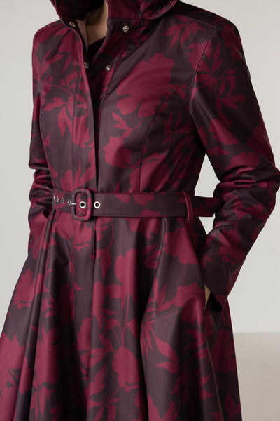 A close-up of a long-sleeve hooded coat with a dark floral pattern in deep burgundy and dark brown, featuring a matching belt with silver-tone buckle details.