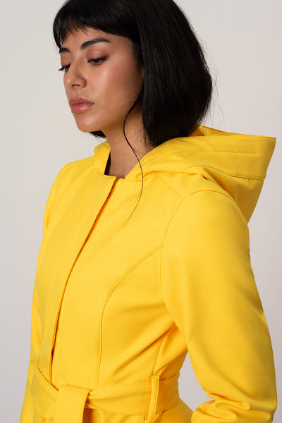 A woman with dark hair wearing RainSisters bright yellow hooded jacket Yellow Sun, shown in a side profile against a plain light gray background.