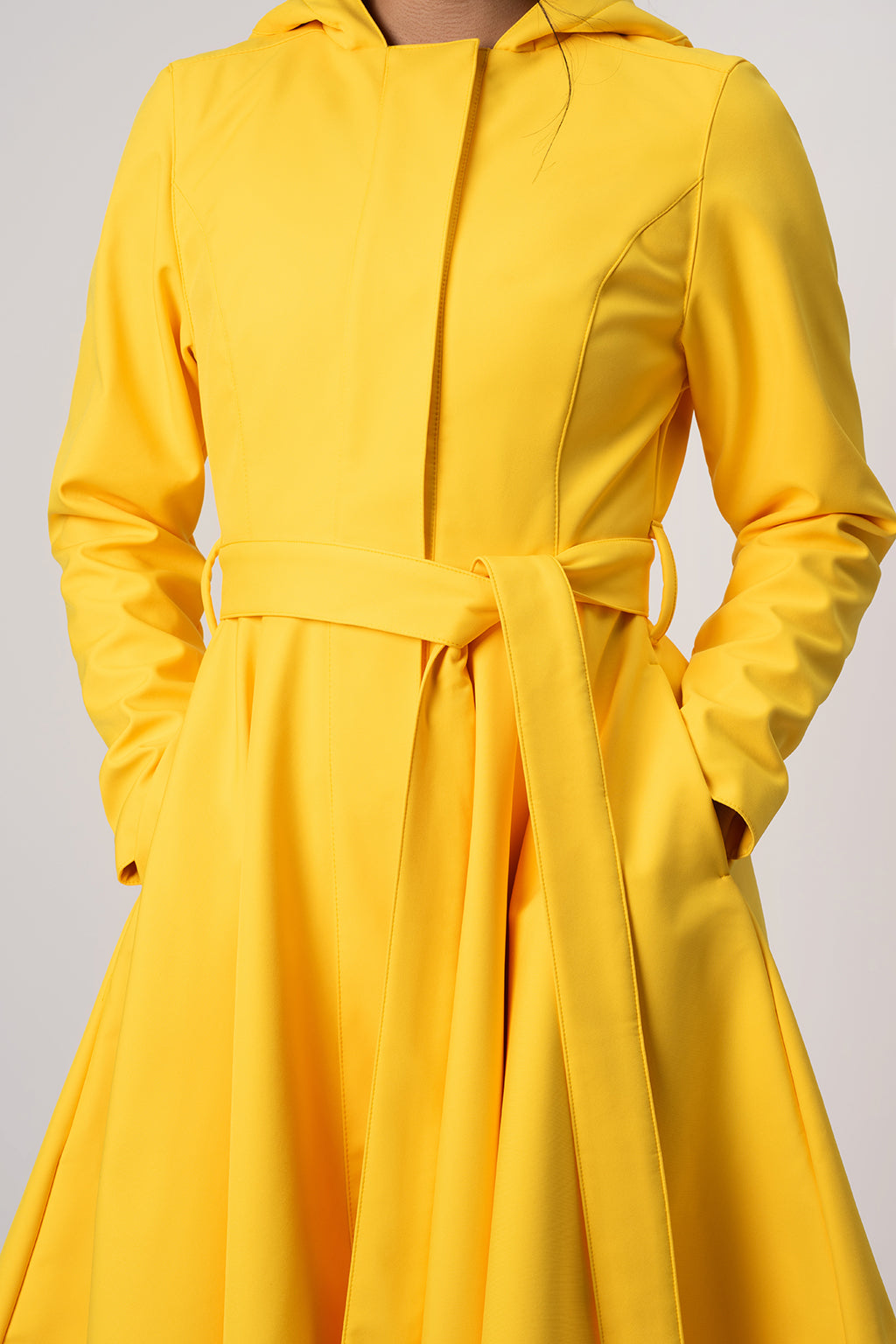 RainSisters bright yellow hooded coat Yellow Sun with a matching waist tie belt, shown on a model against a light gray studio background.