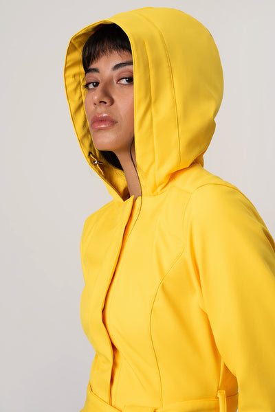 A woman wearing RainSisters bright yellow hooded jacket Yellow Sun, shown in a close-up side profile against a plain light gray studio background.