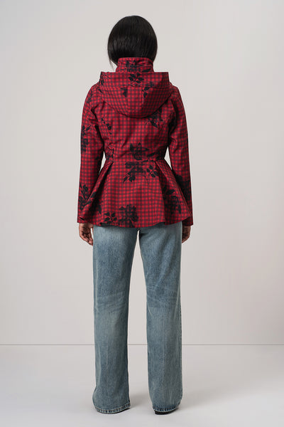 A model viewed from the back wearing RainSisters red and black checkered hooded jacket Crimson Heart with a black floral pattern, paired with light blue jeans, against a plain light gray background.