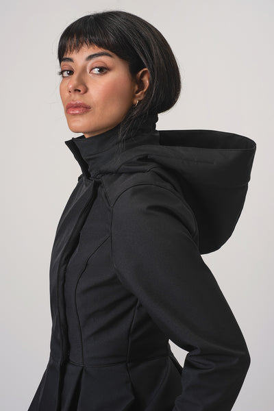 A woman with dark hair is shown in profile wearing RainSisters black hooded jacket Moonlit Bow against a plain light gray studio background.