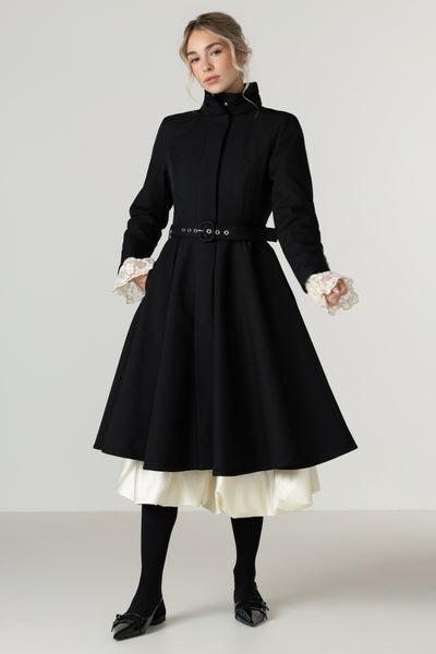 A woman models a Rainsisters black high-neck, long-sleeve A-line winter coat with a matching waist belt. 