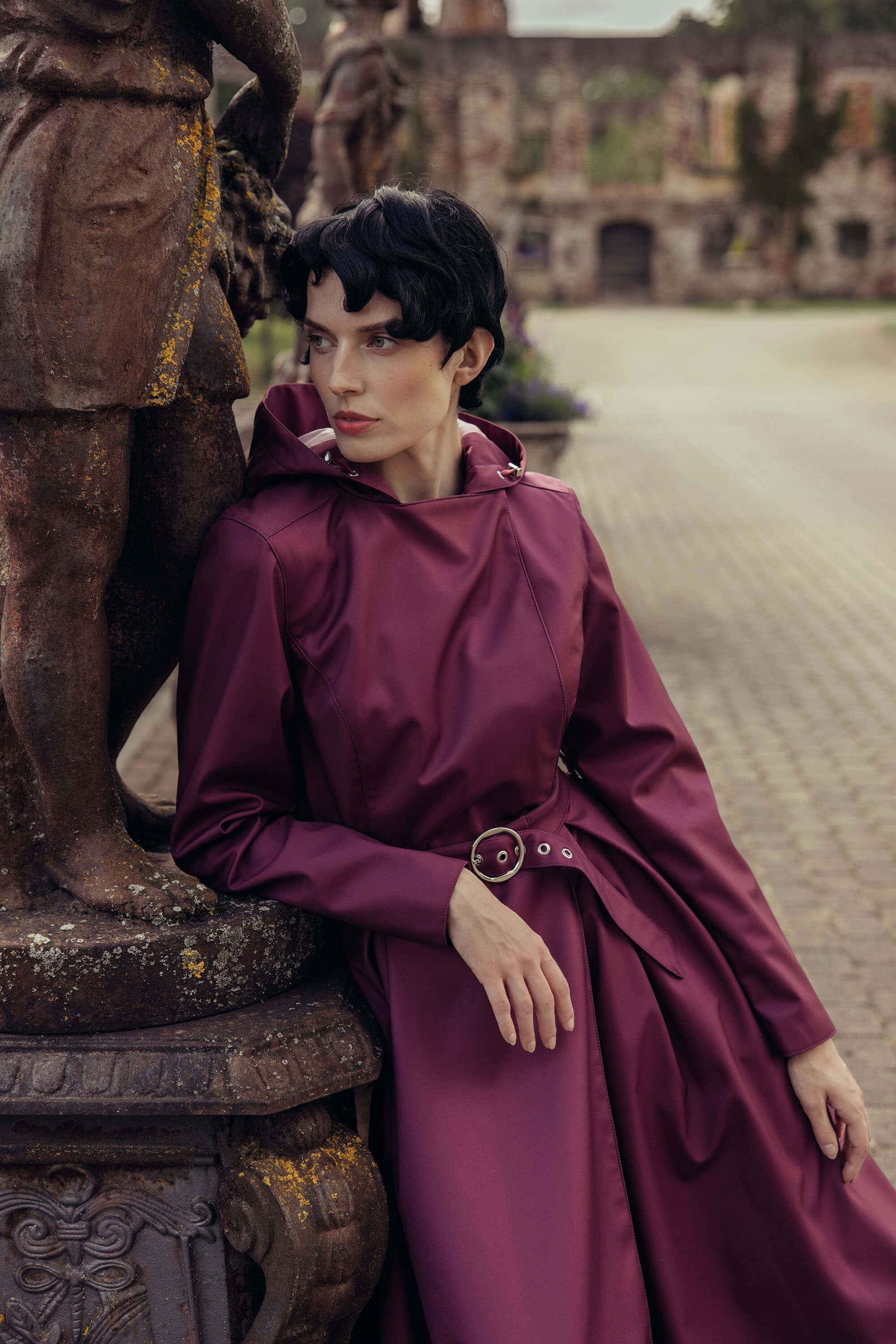 Elegant deep burgundy trench coat with a matching buckle belt styled in a natural outdoor setting.