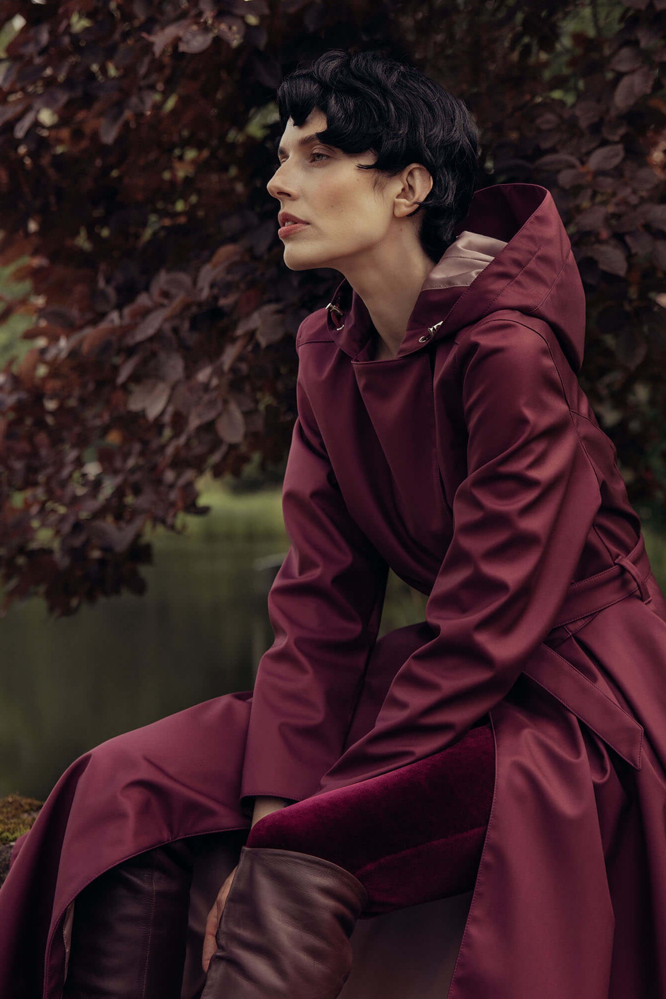 Woman wearing a deep burgundy double-breasted trench coat in a rich berry tone styled outdoors.