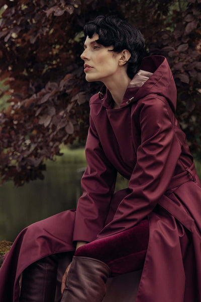 Woman wearing a deep burgundy double-breasted trench coat in a rich berry tone styled outdoors.