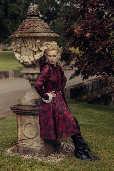 Woman wearing a burgundy floral fit and flare coat with a full circle skirt styled outdoors in an elegant autumn setting.