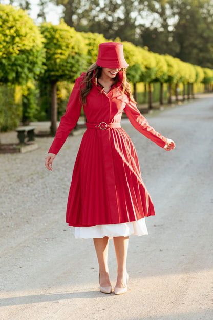 Woman in a red coat and red hat standing on a road with greenery in the background