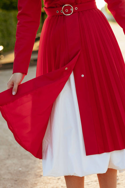 Red coat with a belt over a white dress, outdoor background.
