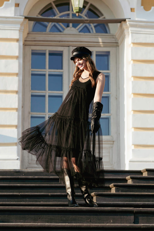 Woman in a black evening tulle dress and hat standing on steps in front of a building