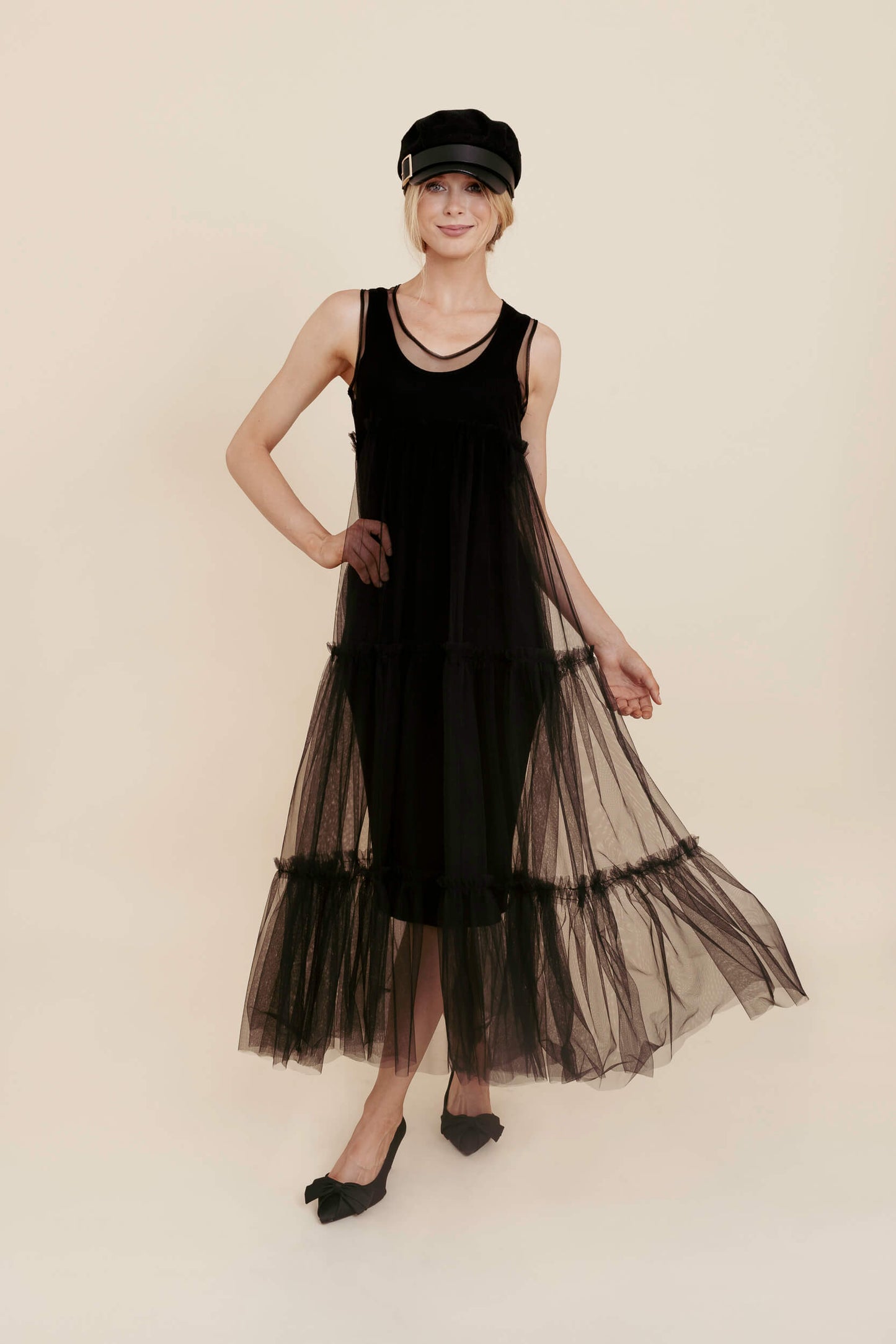 Woman wearing a black sleeveless dress with sheer overlay on a beige background