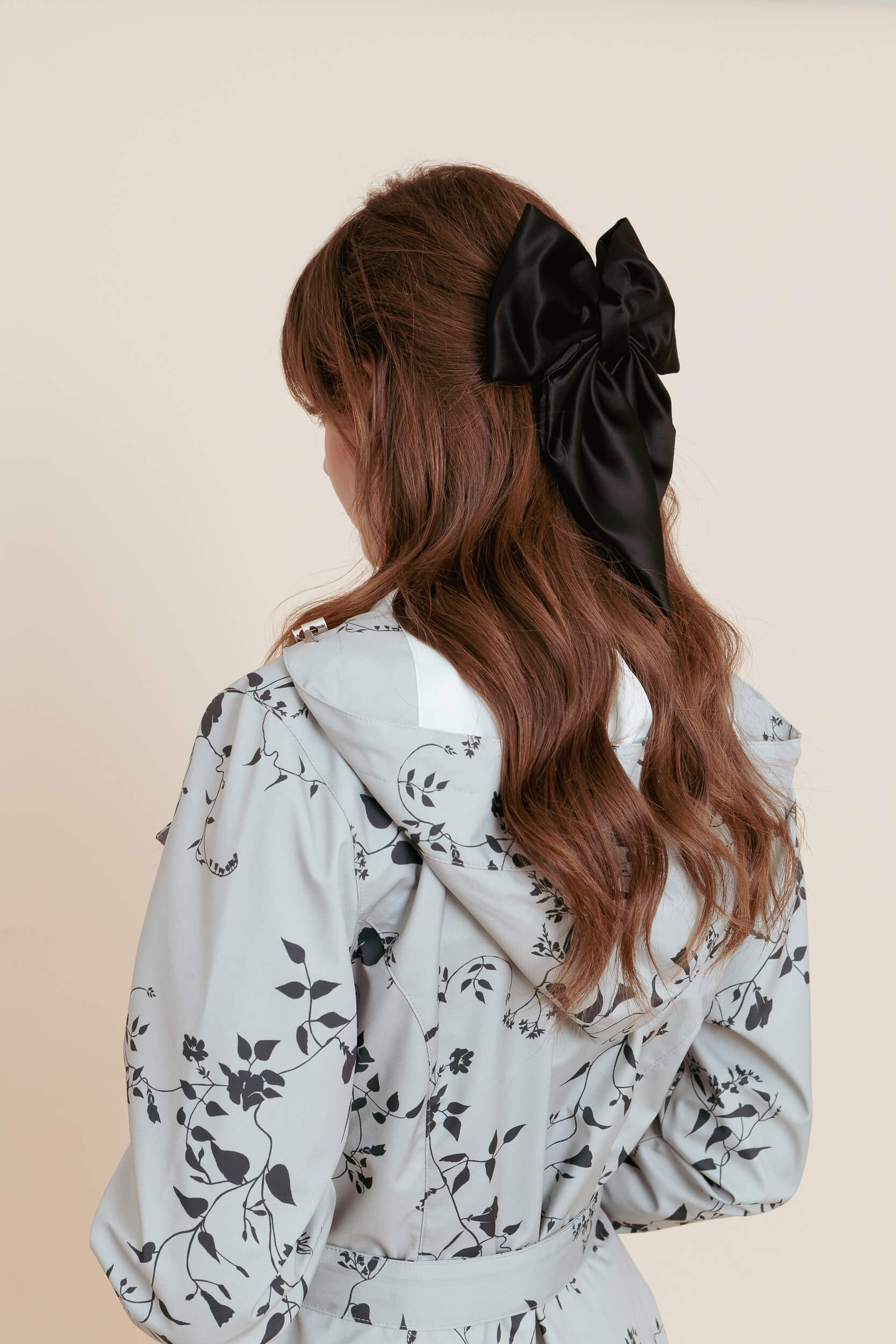 Model wearing a floral minty coat with a black hair bow on a beige background
